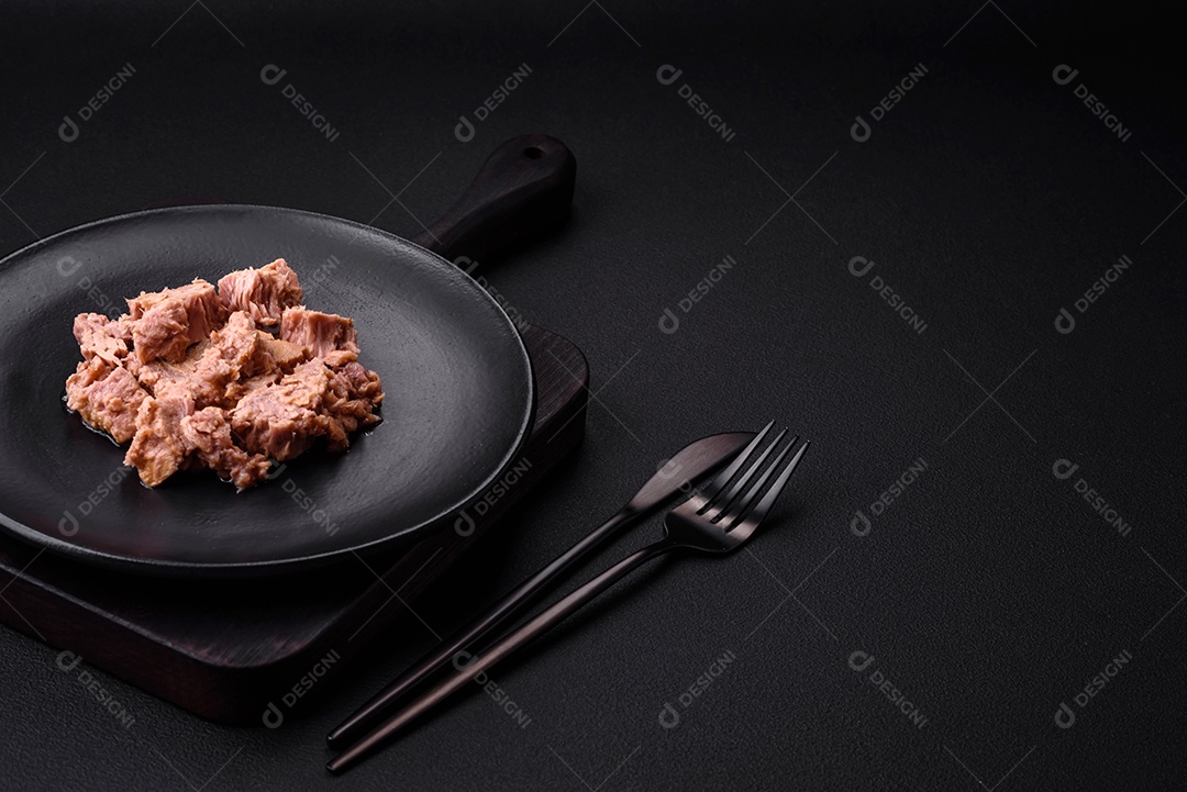 Deliciosa carne de atum enlatada em uma placa de cerâmica preta sobre um fundo escuro de concreto. Preparação de alimentos saudáveis