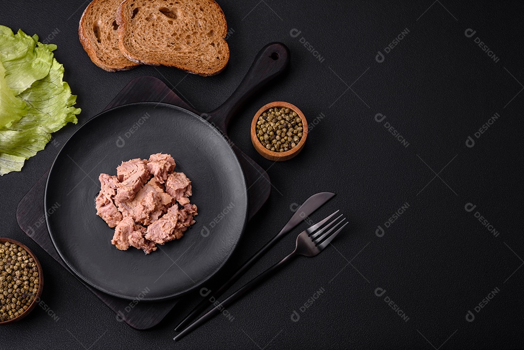 Deliciosa carne de atum enlatada em uma placa de cerâmica preta sobre um fundo escuro de concreto. Preparação de alimentos saudáveis