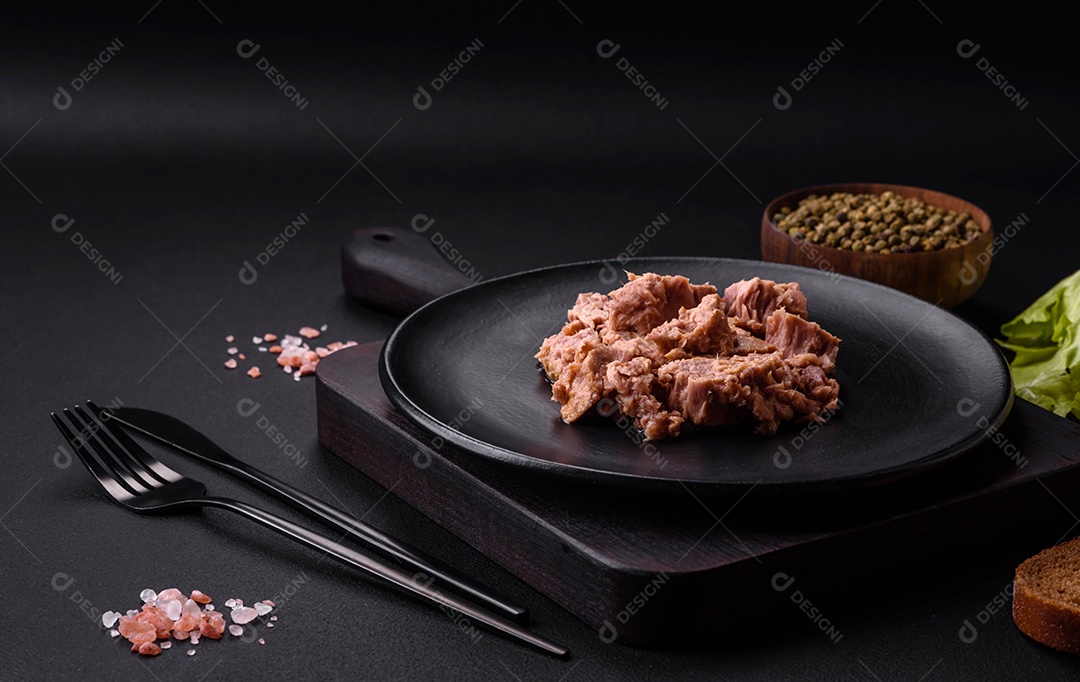 Deliciosa carne de atum enlatada em uma placa de cerâmica preta sobre um fundo escuro de concreto. Preparação de alimentos saudáveis