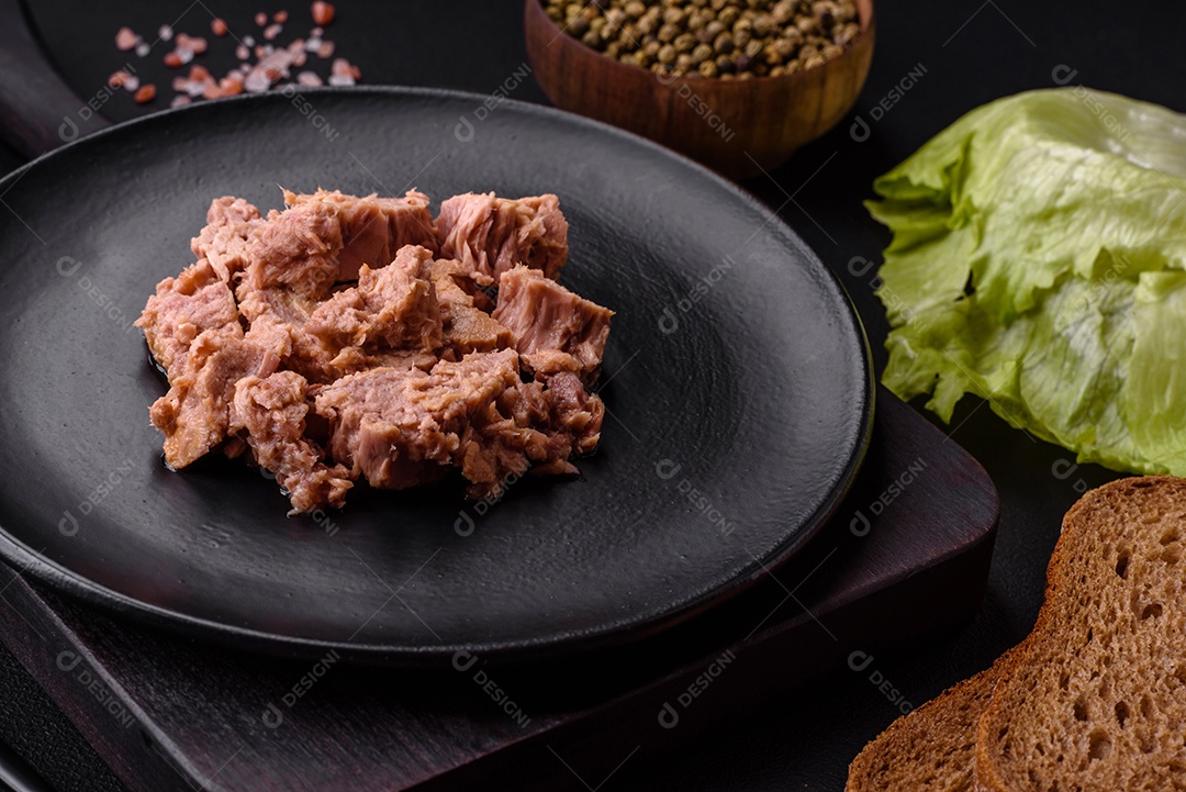 Deliciosa carne de atum enlatada em uma placa de cerâmica preta sobre um fundo escuro de concreto. Preparação de alimentos saudáveis