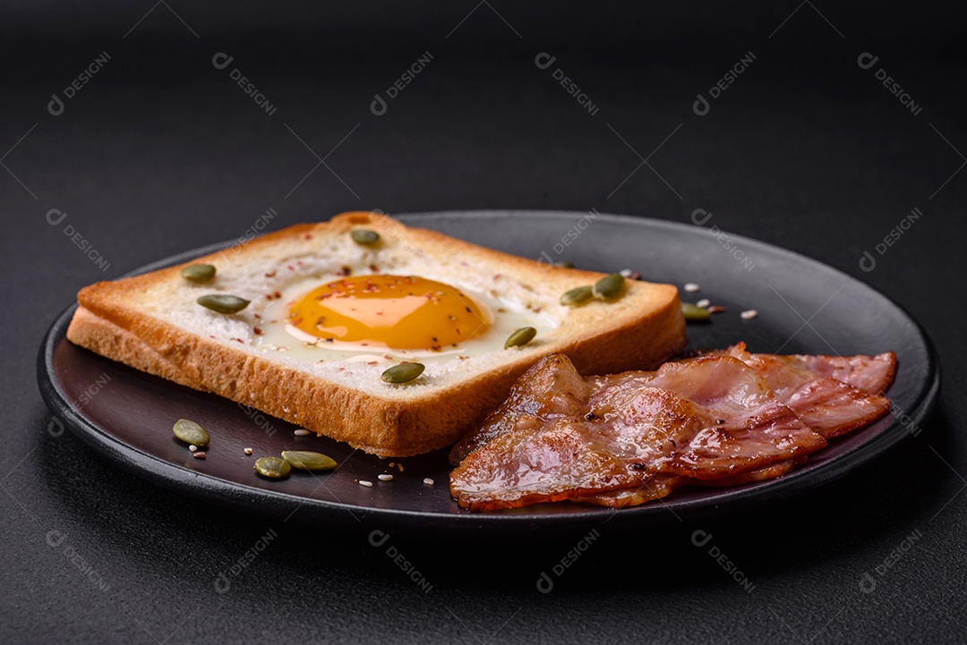 Ovo frito em forma de coração em torradas de pão com sementes de gergelim, sementes de linho e sementes de abóbora em uma placa preta sobre um fundo escuro de concreto