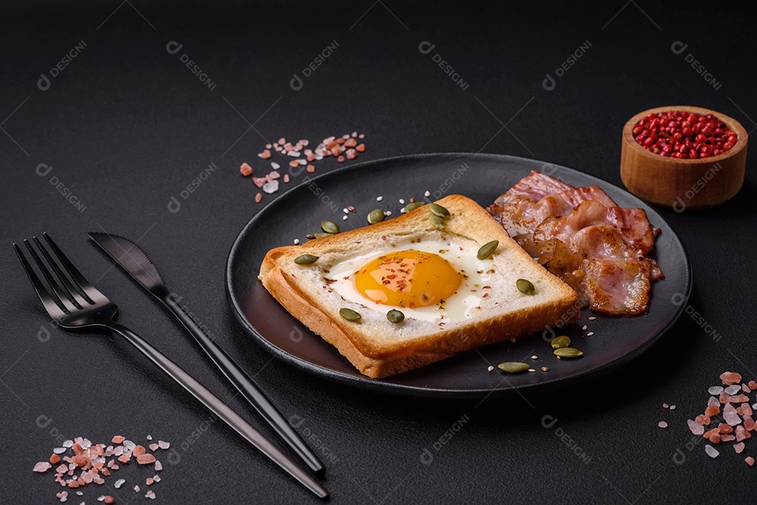Ovo frito em forma de coração em torradas de pão com sementes de gergelim, sementes de linho e sementes de abóbora em uma placa preta sobre um fundo escuro de concreto