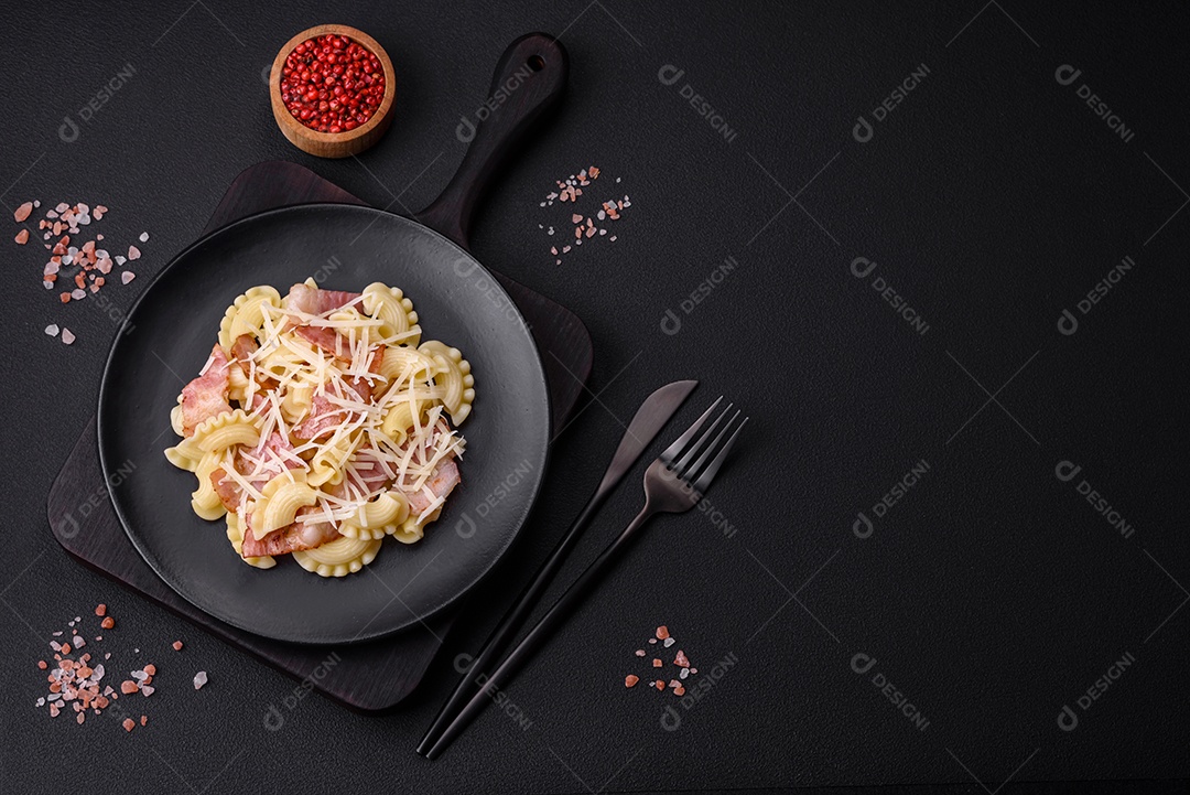 Deliciosa massa com bacon e queijo parmesão em uma placa de cerâmica preta sobre um fundo escuro de concreto. Prato da culinária italiana
