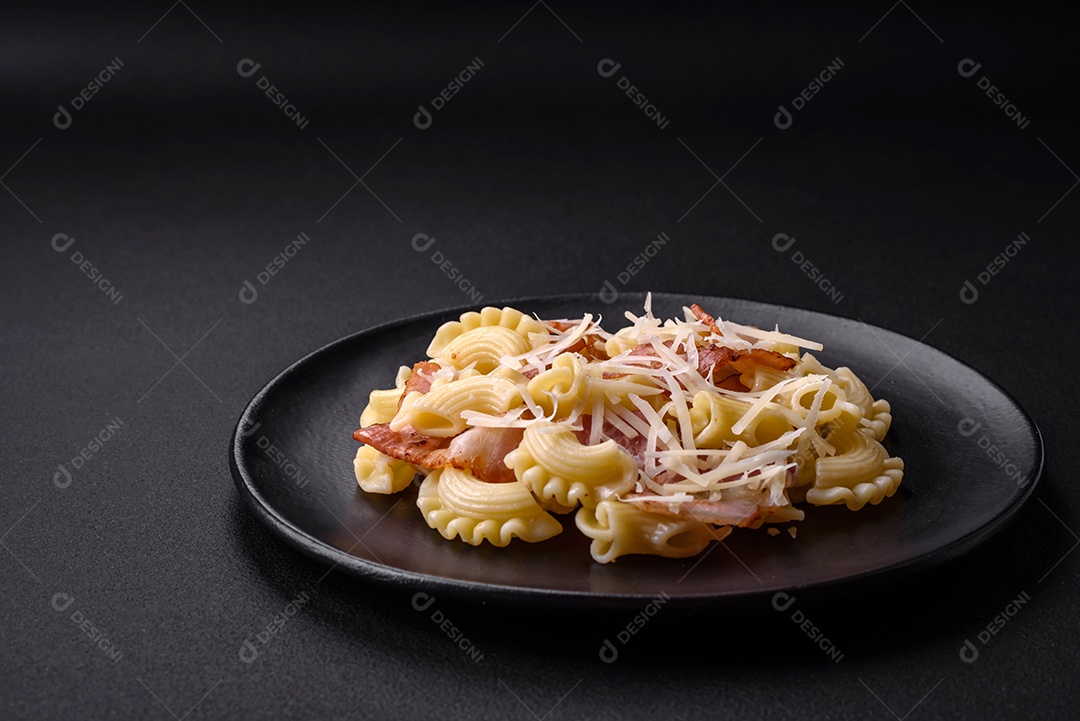 Deliciosa massa com bacon e queijo parmesão em uma placa de cerâmica preta sobre um fundo escuro de concreto. Prato da culinária italiana