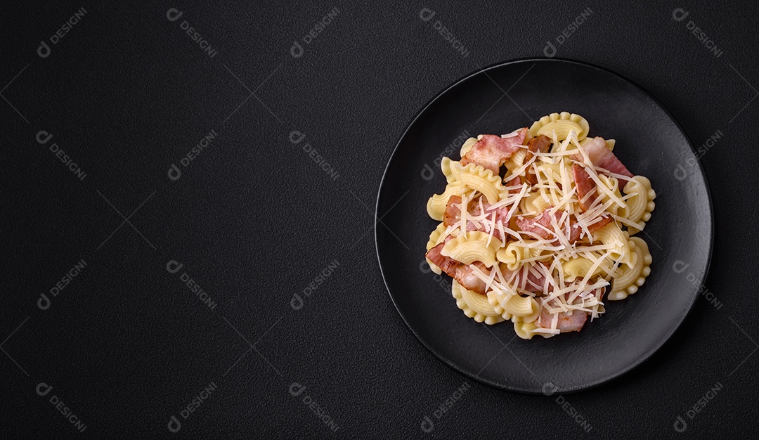 Deliciosa massa com bacon e queijo parmesão em uma placa de cerâmica preta sobre um fundo escuro de concreto. Prato da culinária italiana