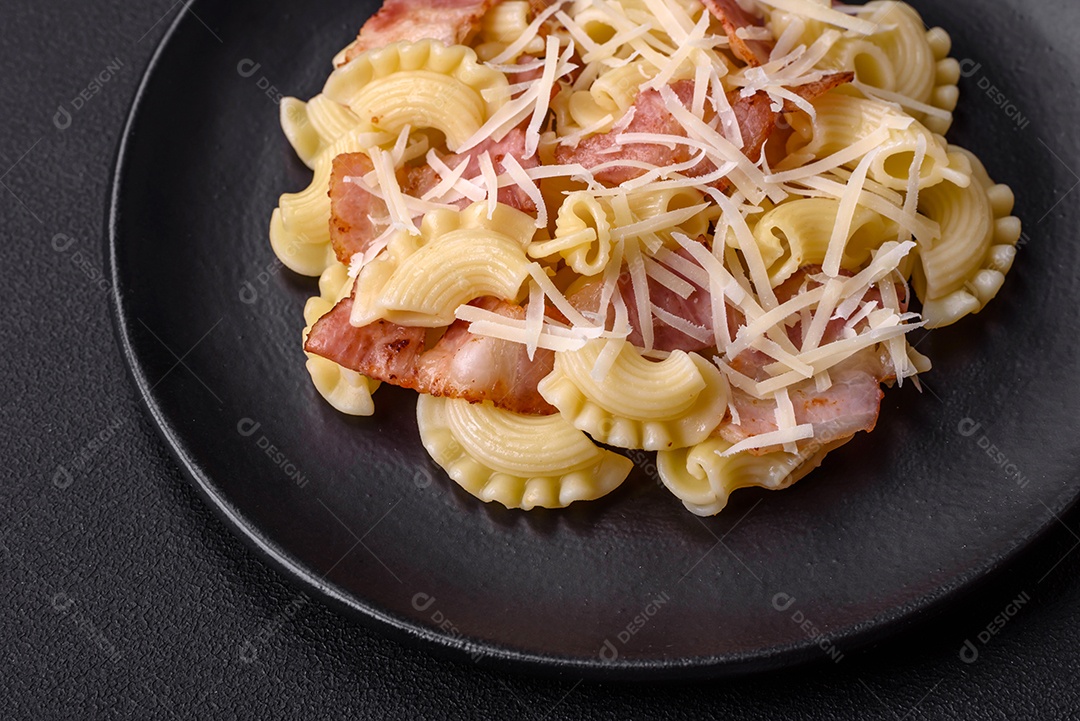 Deliciosa massa com bacon e queijo parmesão em uma placa de cerâmica preta sobre um fundo escuro de concreto. Prato da culinária italiana