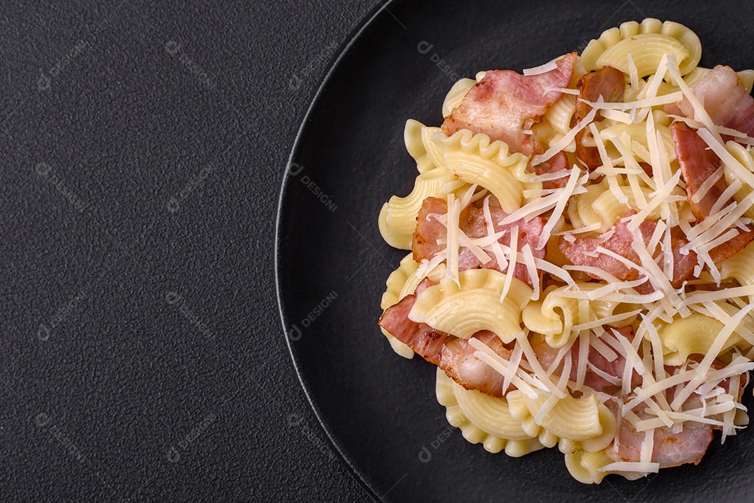 Deliciosa massa com bacon e queijo parmesão em uma placa de cerâmica preta sobre um fundo escuro de concreto. Prato da culinária italiana