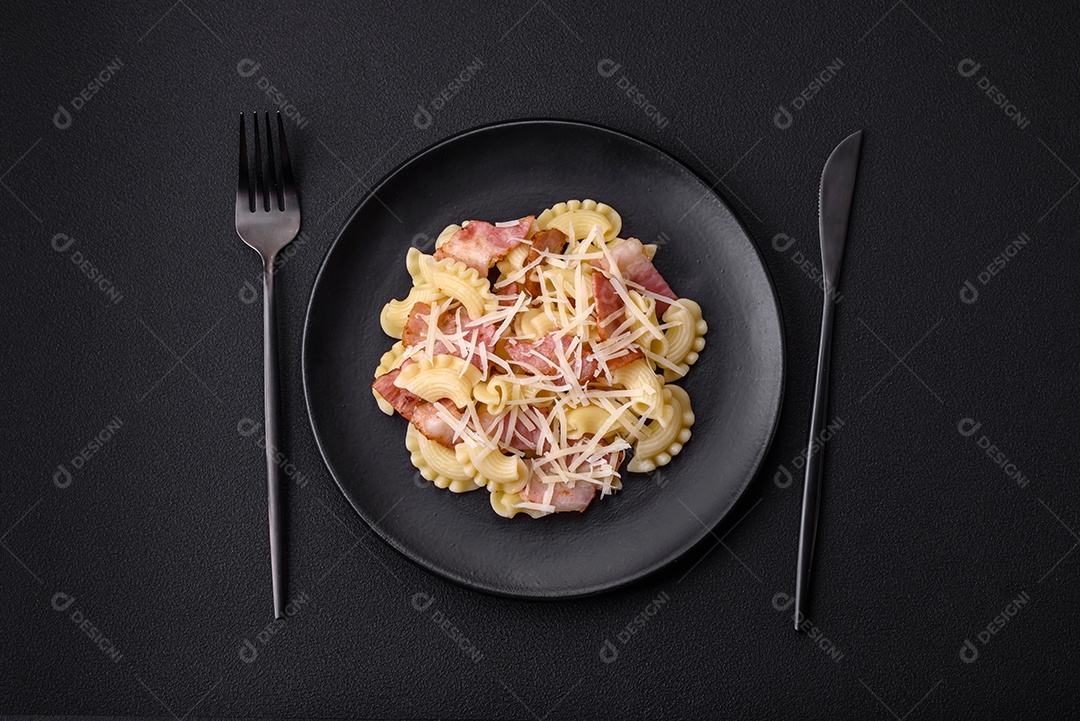 Deliciosa massa com bacon e queijo parmesão em uma placa de cerâmica preta sobre um fundo escuro de concreto. Prato da culinária italiana