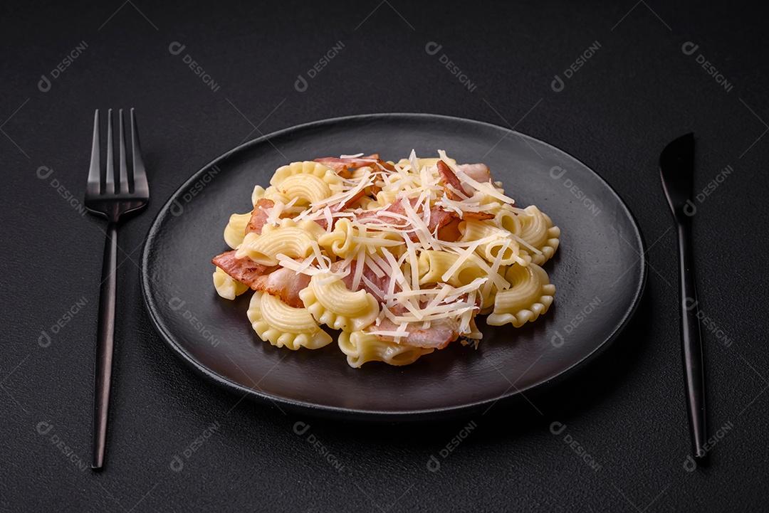 Deliciosa massa com bacon e queijo parmesão em uma placa de cerâmica preta sobre um fundo escuro de concreto. Prato da culinária italiana