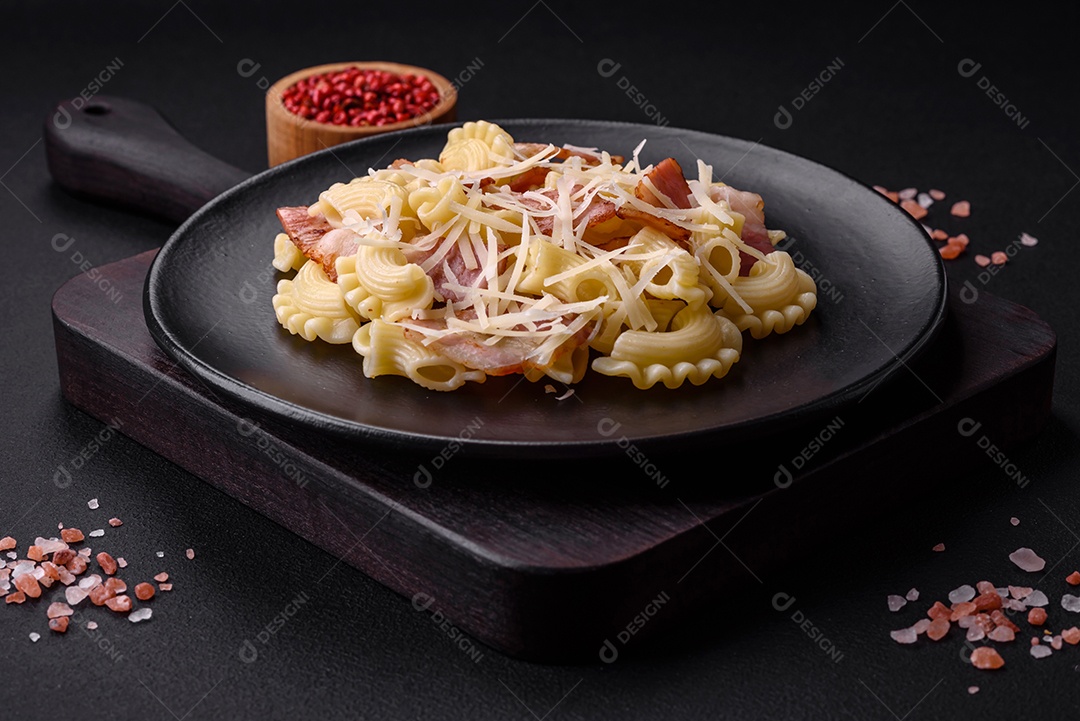 Deliciosa massa com bacon e queijo parmesão em uma placa de cerâmica preta sobre um fundo escuro de concreto. Prato da culinária italiana