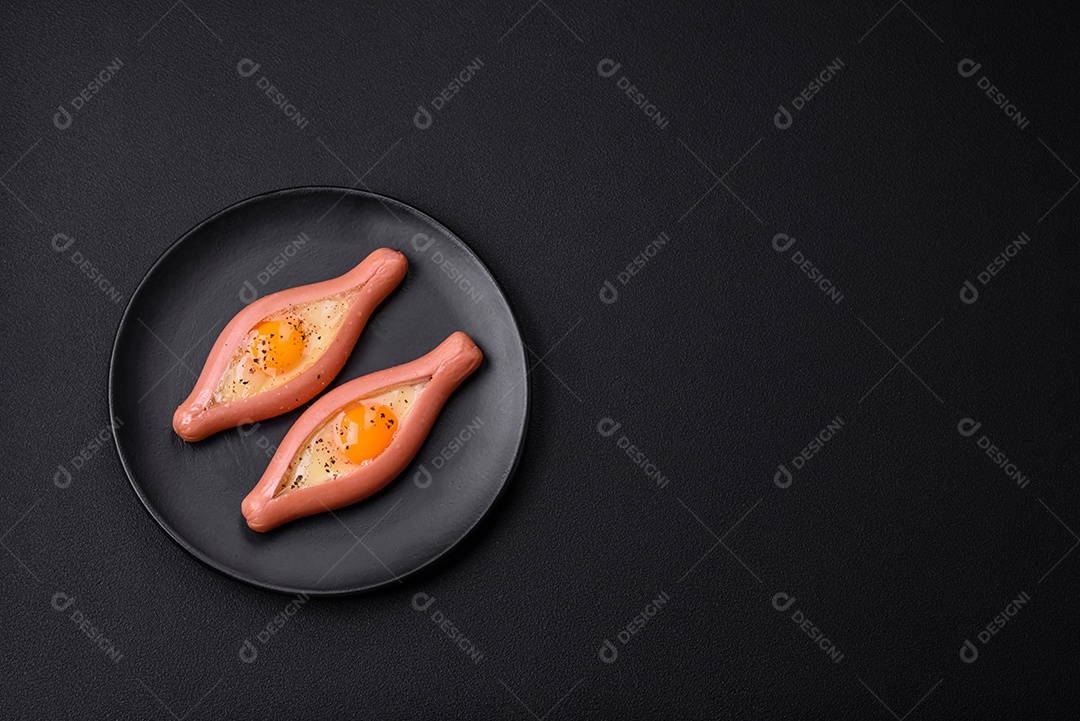 Conceito composto de ovos fritos dentro de uma salsicha cortada com especiarias em uma placa de cerâmica preta sobre um fundo escuro de concreto