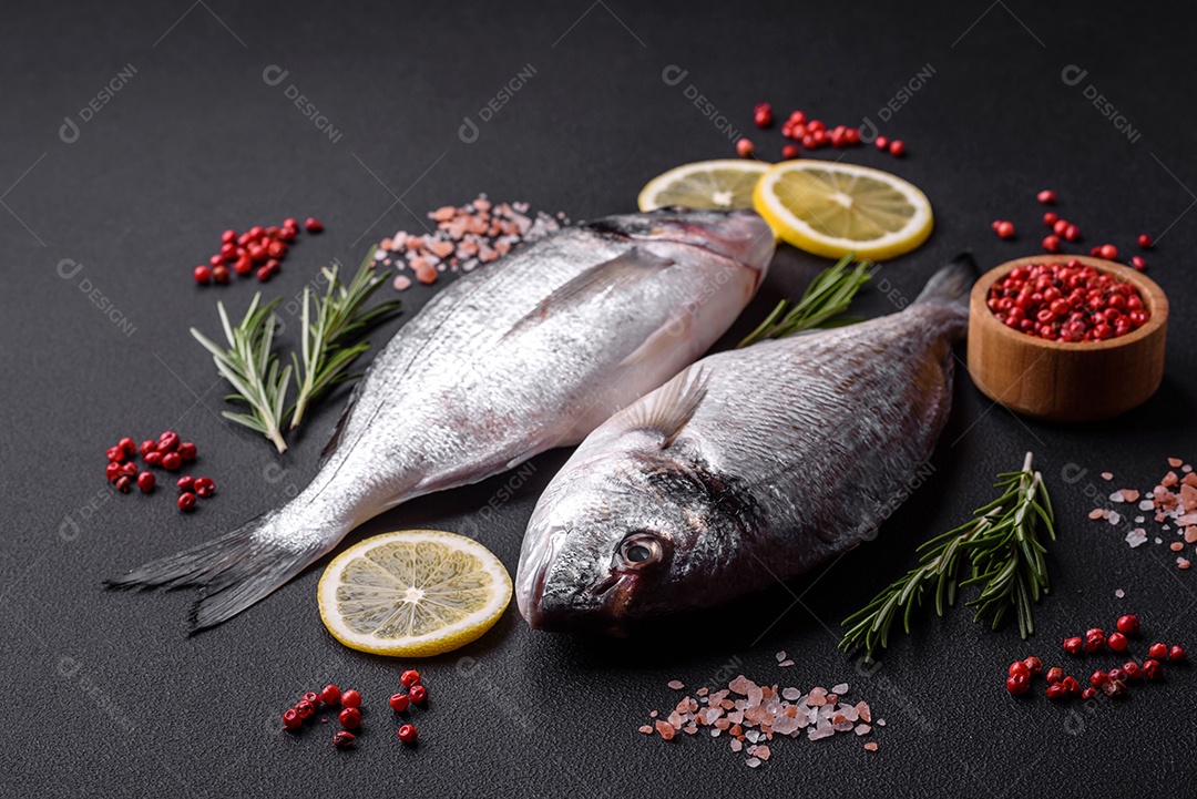 Peixe dourado cru fresco com especiarias, ervas, sal e limão sobre um fundo escuro de concreto