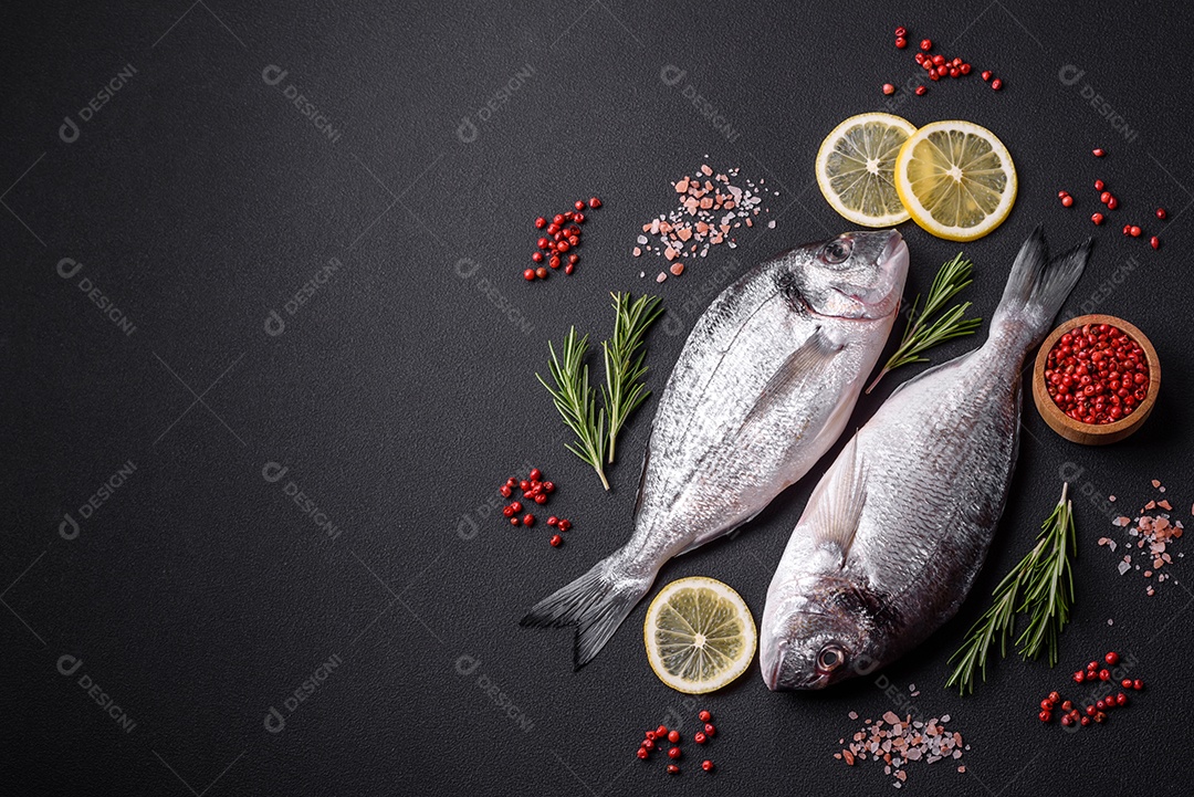 Peixe dourado cru fresco com especiarias, ervas, sal e limão sobre um fundo escuro de concreto