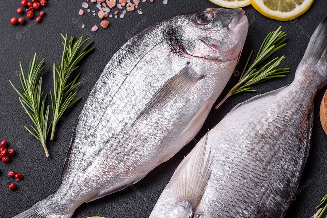 Peixe dourado cru fresco com especiarias, ervas, sal e limão sobre um fundo escuro de concreto