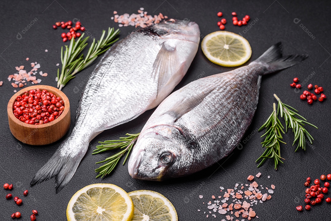 Peixe dourado cru fresco com especiarias, ervas, sal e limão sobre um fundo escuro de concreto