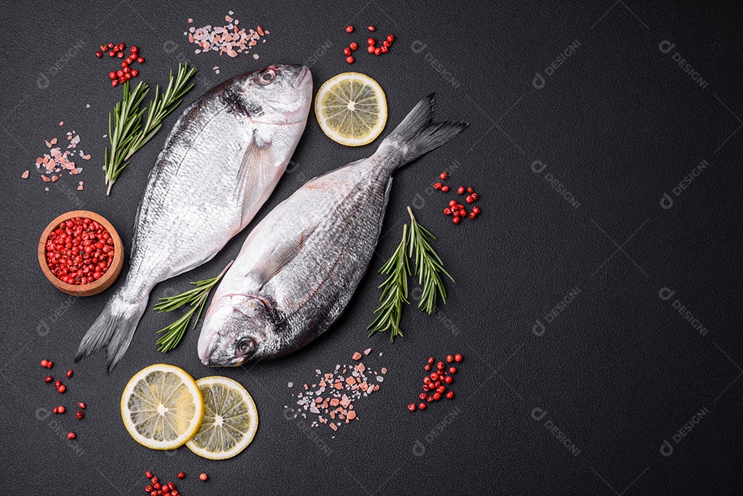 Peixe dourado cru fresco com especiarias, ervas, sal e limão sobre um fundo escuro de concreto