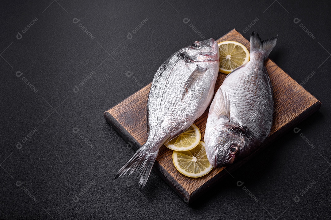 Peixe dourado cru fresco com especiarias, ervas, sal e limão sobre um fundo escuro de concreto