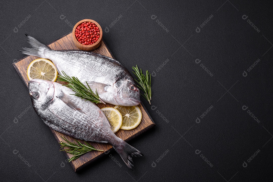 Peixe dourado cru fresco com especiarias, ervas, sal e limão sobre um fundo escuro de concreto