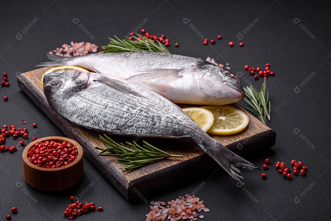 Peixe dourado cru fresco com especiarias, ervas, sal e limão sobre um fundo escuro de concreto