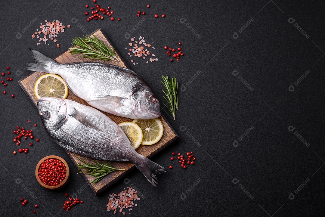 Peixe dourado cru fresco com especiarias, ervas, sal e limão sobre um fundo escuro de concreto