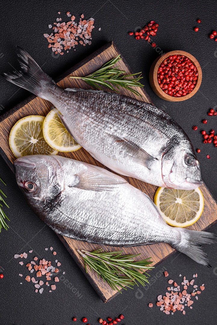 Peixe dourado cru fresco com especiarias, ervas, sal e limão sobre um fundo escuro de concreto