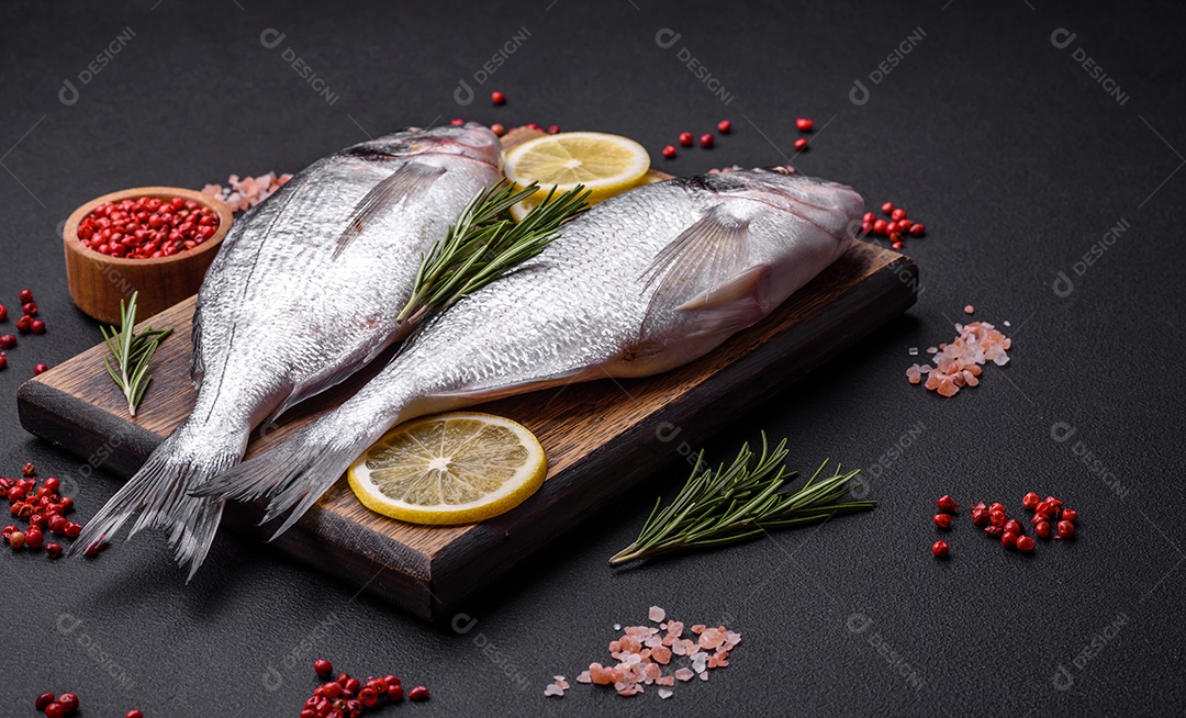 Peixe dourado cru fresco com especiarias, ervas, sal e limão sobre um fundo escuro de concreto
