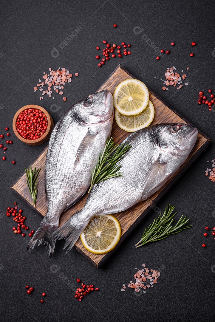 Peixe dourado cru fresco com especiarias, ervas, sal e limão sobre um fundo escuro de concreto