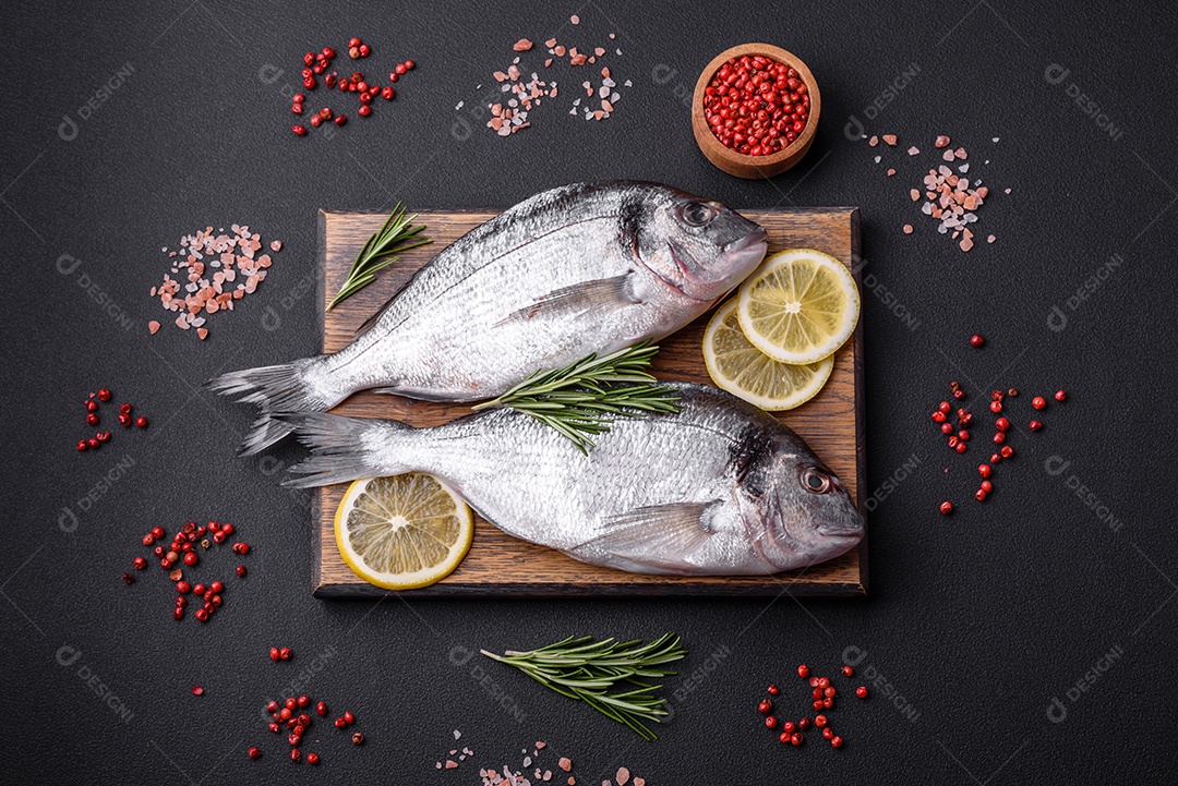 Peixe dourado cru fresco com especiarias, ervas, sal e limão sobre um fundo escuro de concreto