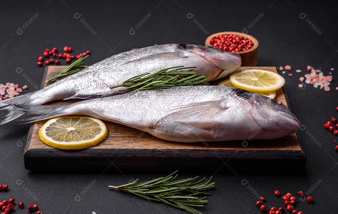 Peixe dourado cru fresco com especiarias, ervas, sal e limão sobre um fundo escuro de concreto