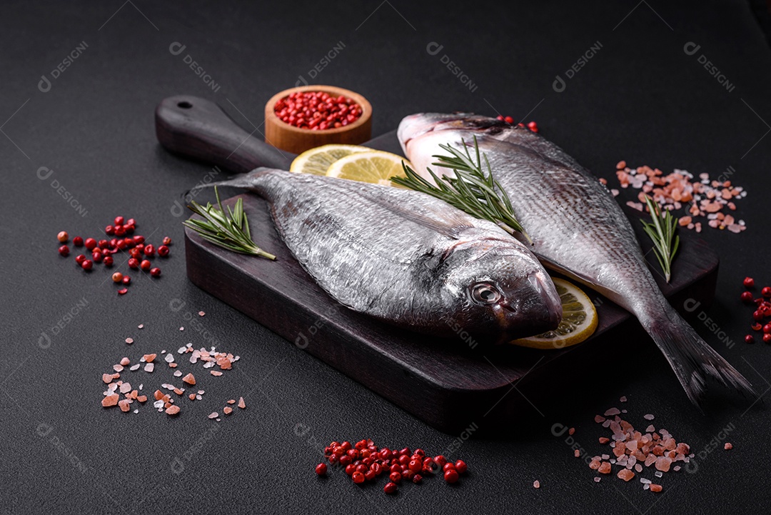 Peixe dourado cru fresco com especiarias, ervas, sal e limão sobre um fundo escuro de concreto