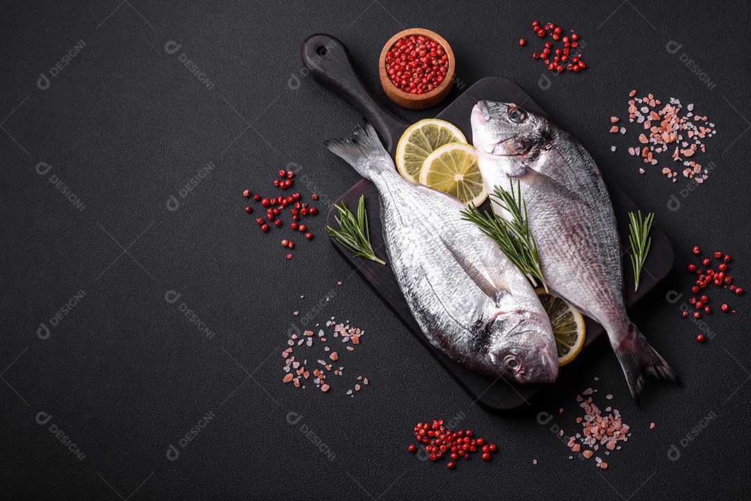 Peixe dourado cru fresco com especiarias, ervas, sal e limão sobre um fundo escuro de concreto