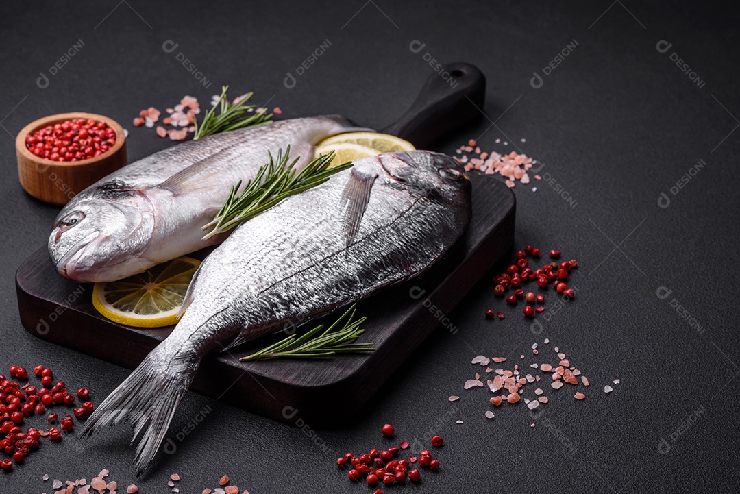 Peixe dourado cru fresco com especiarias, ervas, sal e limão sobre um fundo escuro de concreto