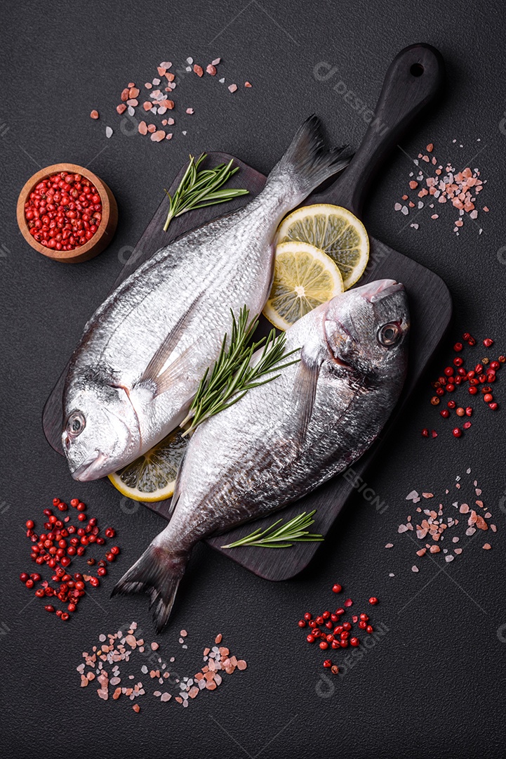 Peixe dourado cru fresco com especiarias, ervas, sal e limão sobre um fundo escuro de concreto