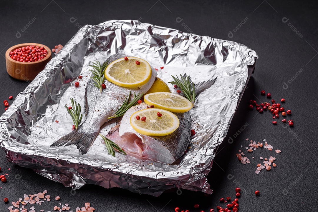 Peixe dourado cru fresco com especiarias, ervas, sal e limão sobre um fundo escuro de concreto