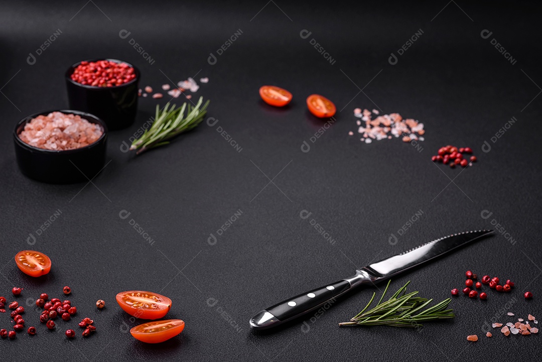 Ingredientes sal, especiarias, ervas e tomates sobre um fundo escuro de concreto.