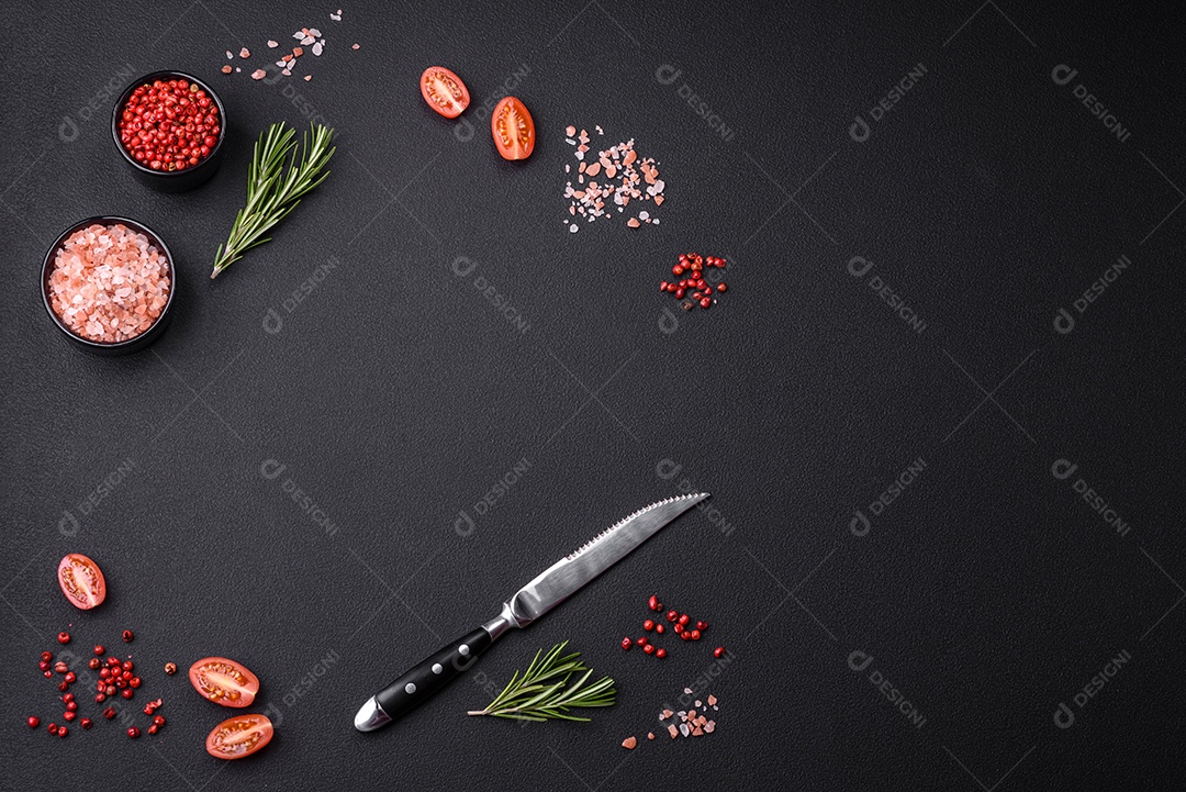 Ingredientes sal, especiarias, ervas e tomates sobre um fundo escuro de concreto.