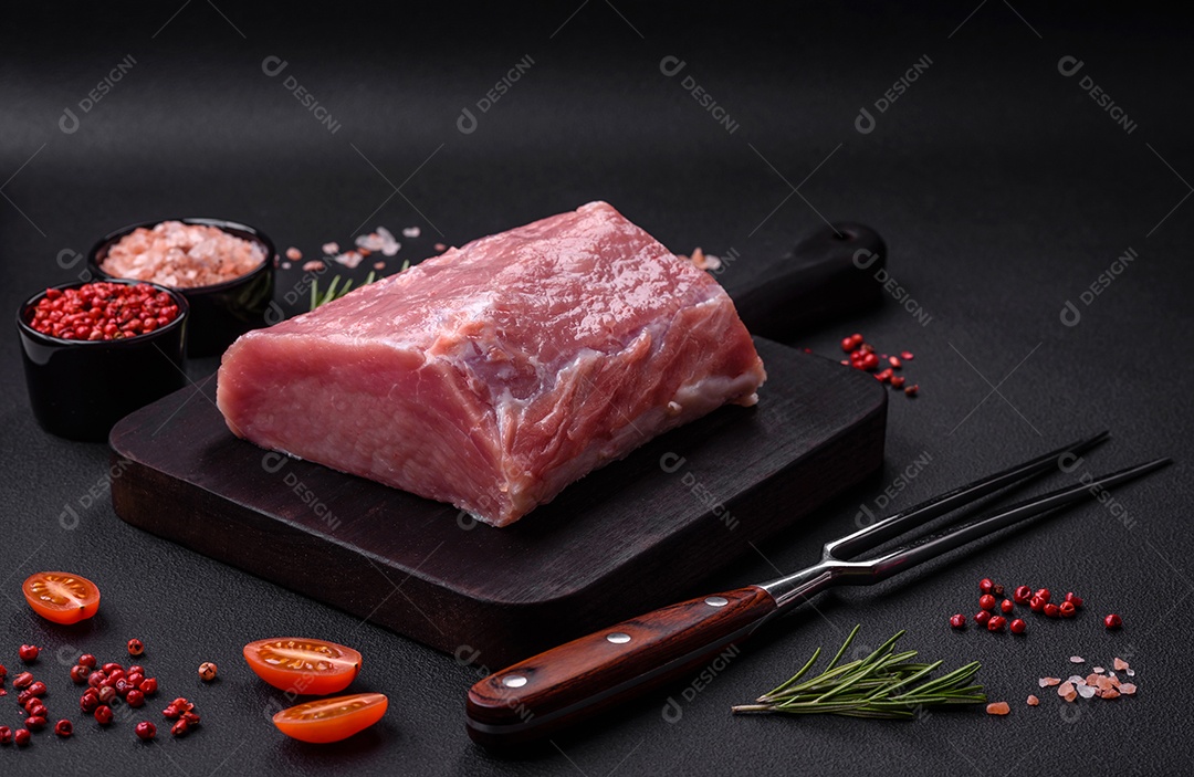 Um pedaço de carne de porco fresca crua sobre uma tábua de madeira com especiarias e ervas sobre um fundo escuro de concreto