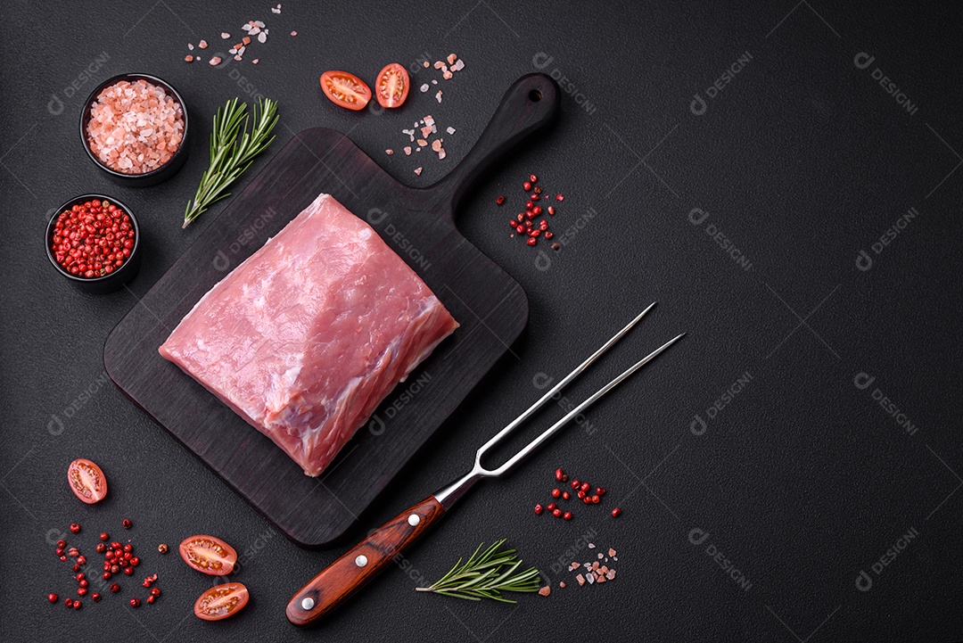 Um pedaço de carne de porco fresca crua sobre uma tábua de madeira com especiarias e ervas sobre um fundo escuro de concreto