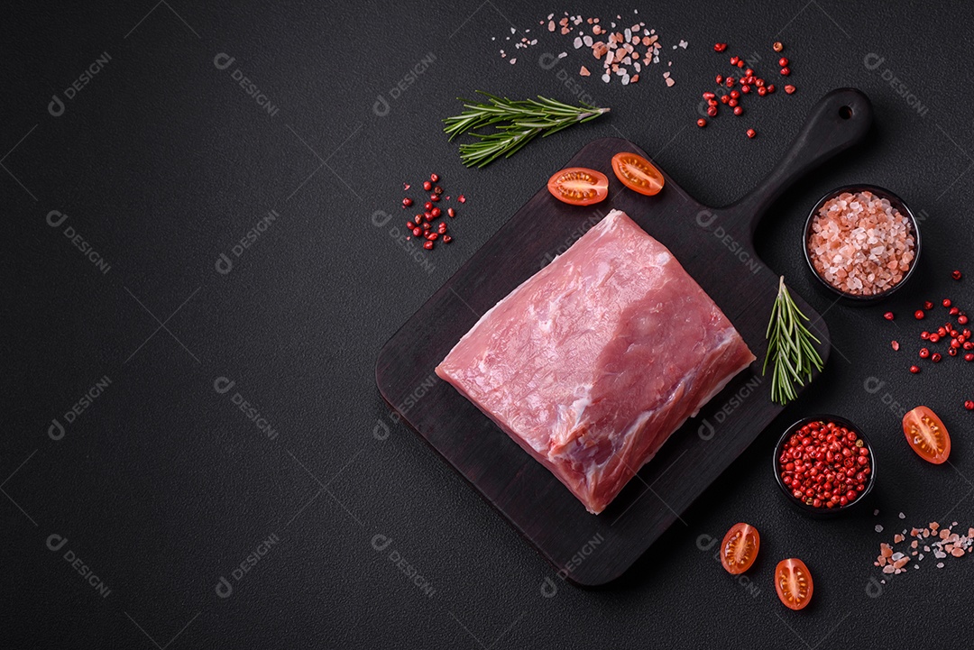 Um pedaço de carne de porco fresca crua sobre uma tábua de madeira com especiarias e ervas sobre um fundo escuro de concreto