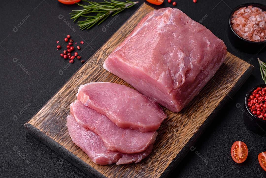 Um pedaço de carne de porco fresca crua sobre uma tábua de madeira com especiarias e ervas sobre um fundo escuro de concreto