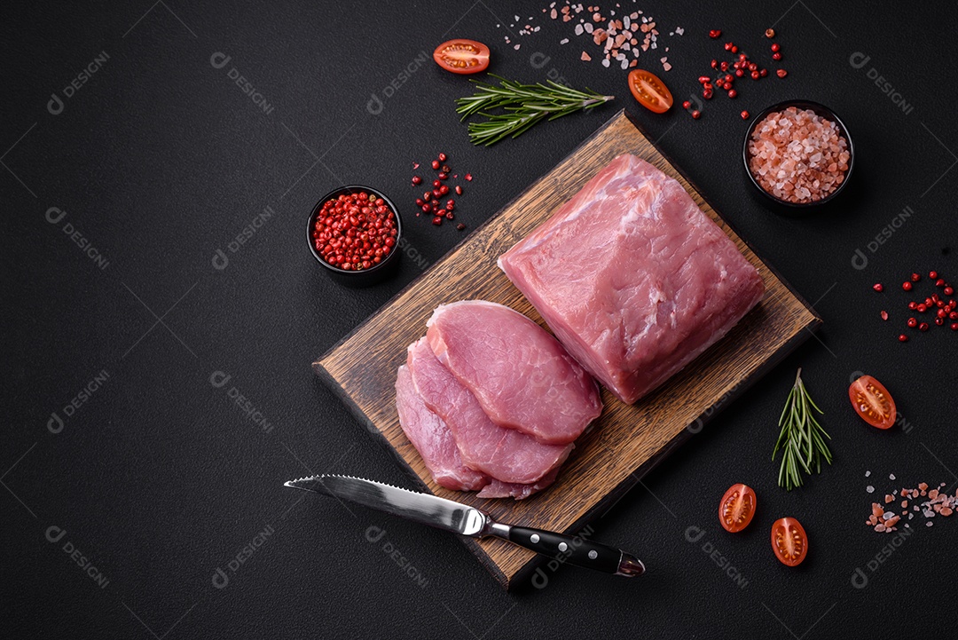 Um pedaço de carne de porco fresca crua sobre uma tábua de madeira com especiarias e ervas sobre um fundo escuro de concreto