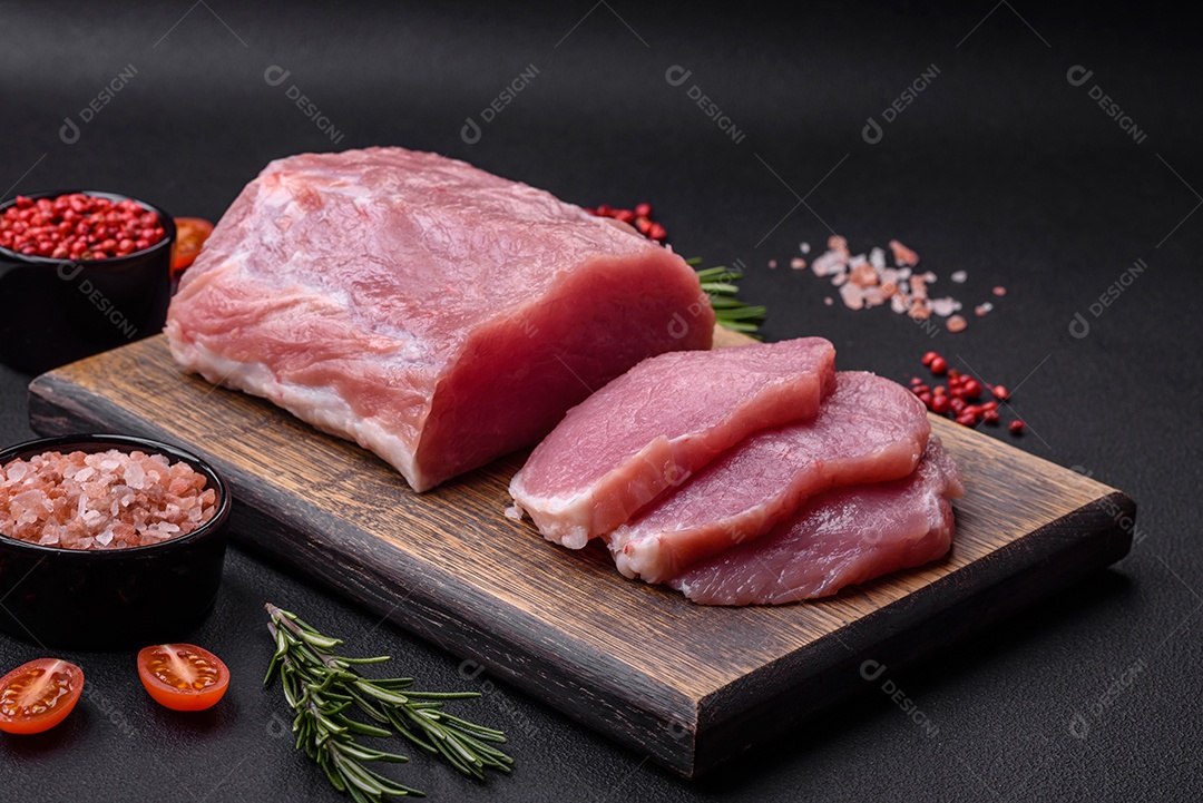 Um pedaço de carne de porco fresca crua sobre uma tábua de madeira com especiarias e ervas sobre um fundo escuro de concreto