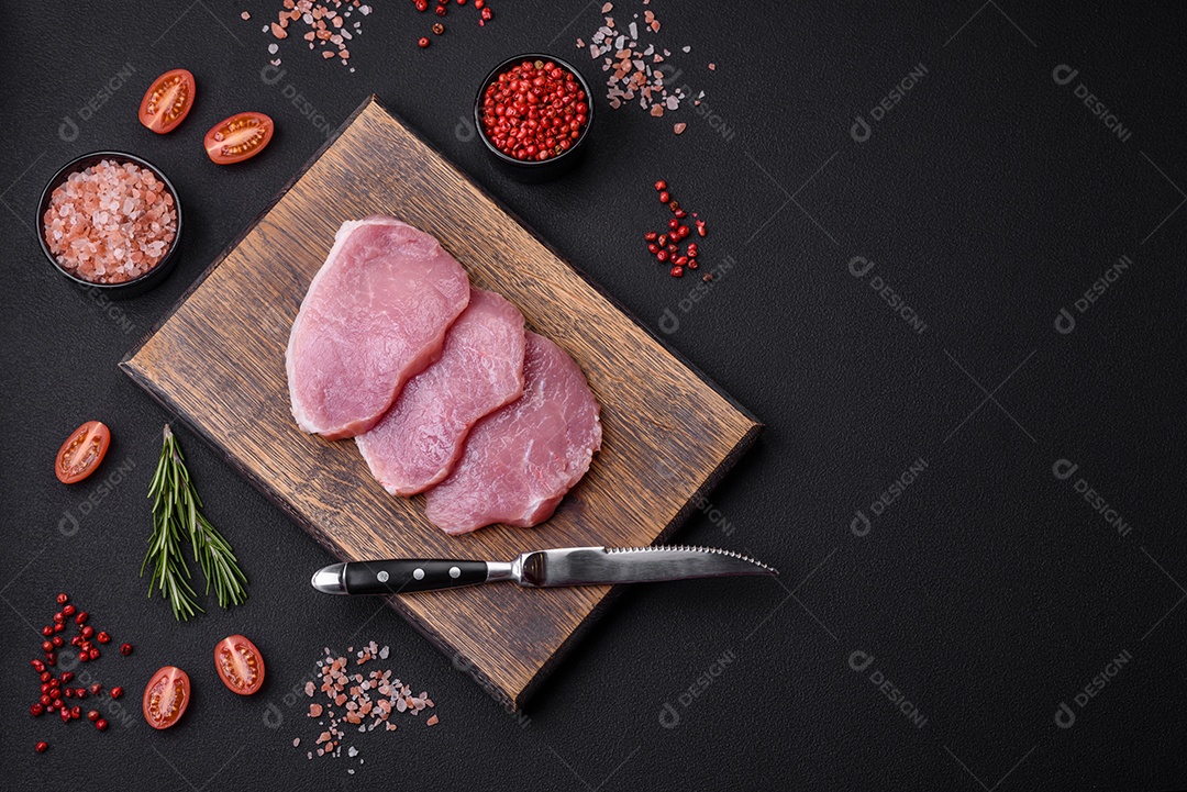 Um pedaço de carne de porco fresca crua sobre uma tábua de madeira com especiarias e ervas sobre um fundo escuro de concreto