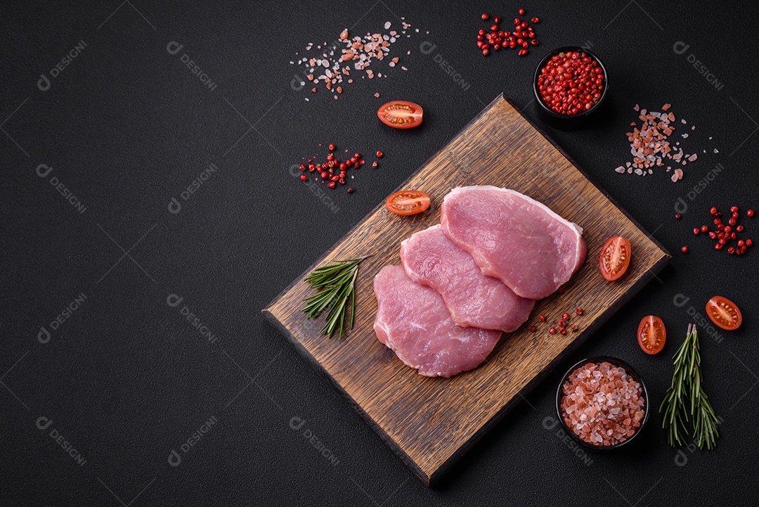 Um pedaço de carne de porco fresca crua sobre uma tábua de madeira com especiarias e ervas sobre um fundo escuro de concreto