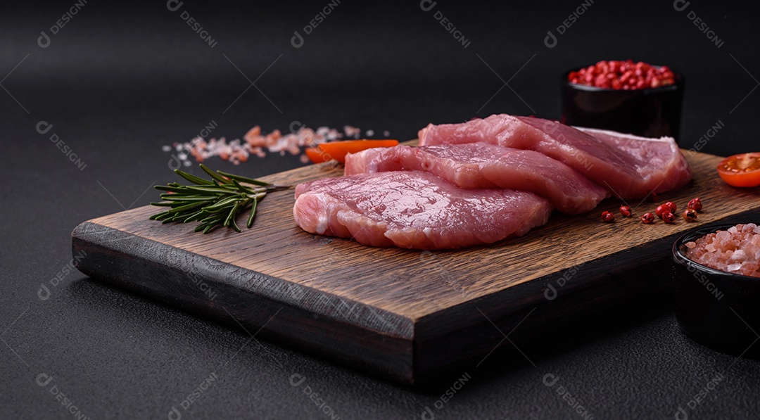 Um pedaço de carne de porco fresca crua sobre uma tábua de madeira com especiarias e ervas sobre um fundo escuro de concreto