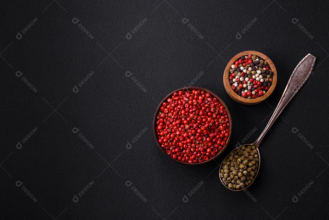 Composição, conceito, consistindo em vários tipos de cores diferentes de pimenta da Jamaica em tigelas e colheres sobre fundo escuro de concreto