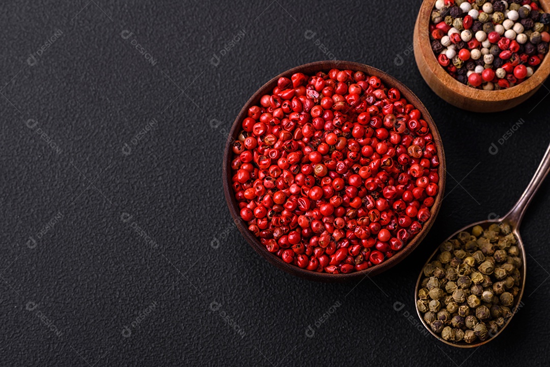 Composição, conceito, consistindo em vários tipos de cores diferentes de pimenta da Jamaica em tigelas e colheres sobre fundo escuro de concreto