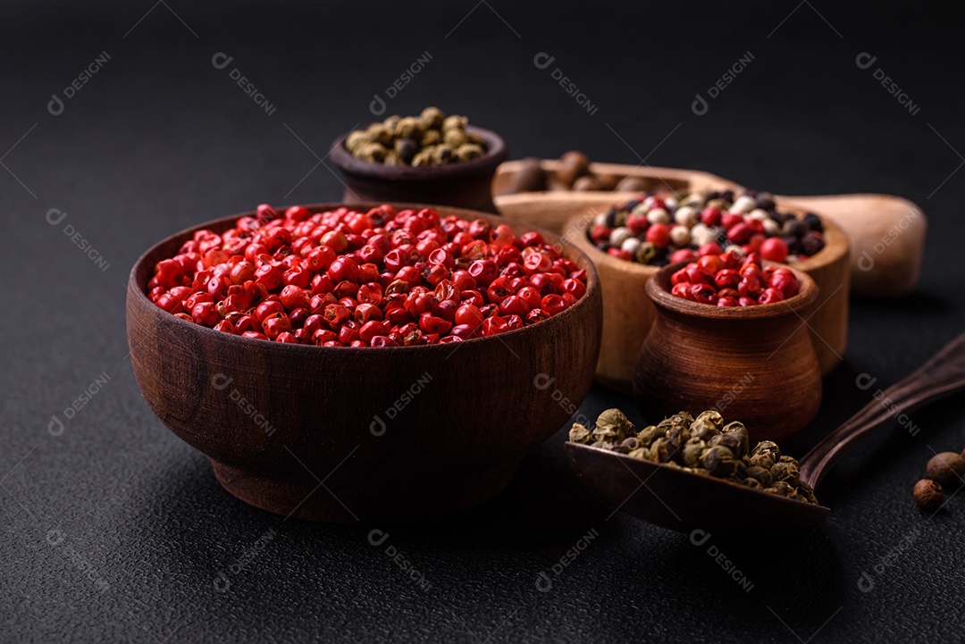 Composição, conceito, consistindo em vários tipos de cores diferentes de pimenta da Jamaica em tigelas e colheres sobre fundo escuro de concreto