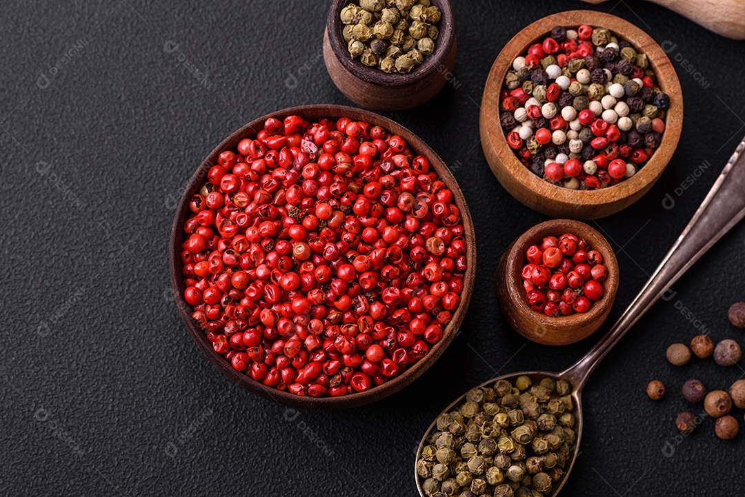 Composição, conceito, consistindo em vários tipos de cores diferentes de pimenta da Jamaica em tigelas e colheres sobre fundo escuro de concreto