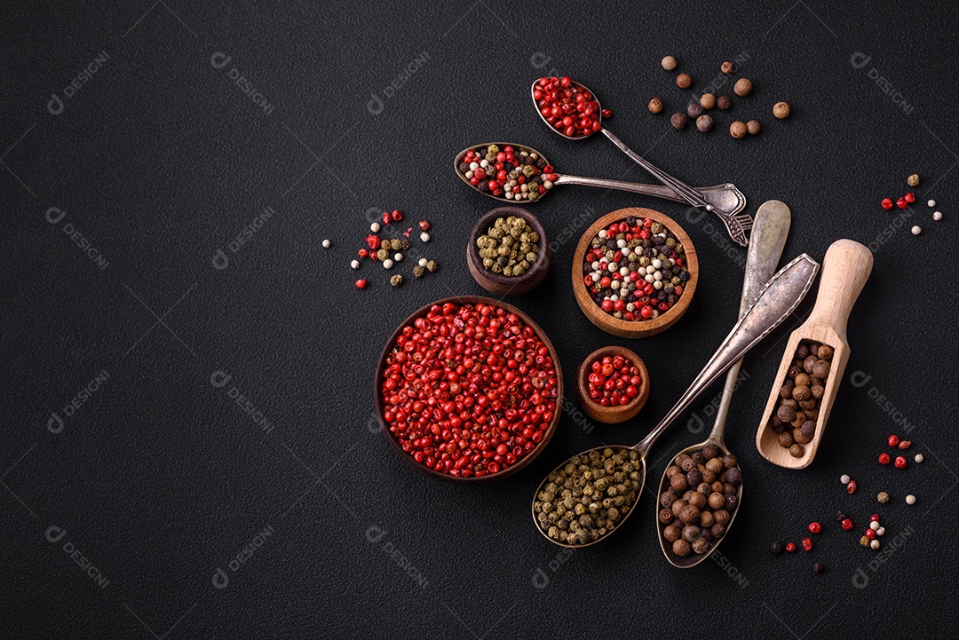 Composição, conceito, consistindo em vários tipos de cores diferentes de pimenta da Jamaica em tigelas e colheres sobre fundo escuro de concreto